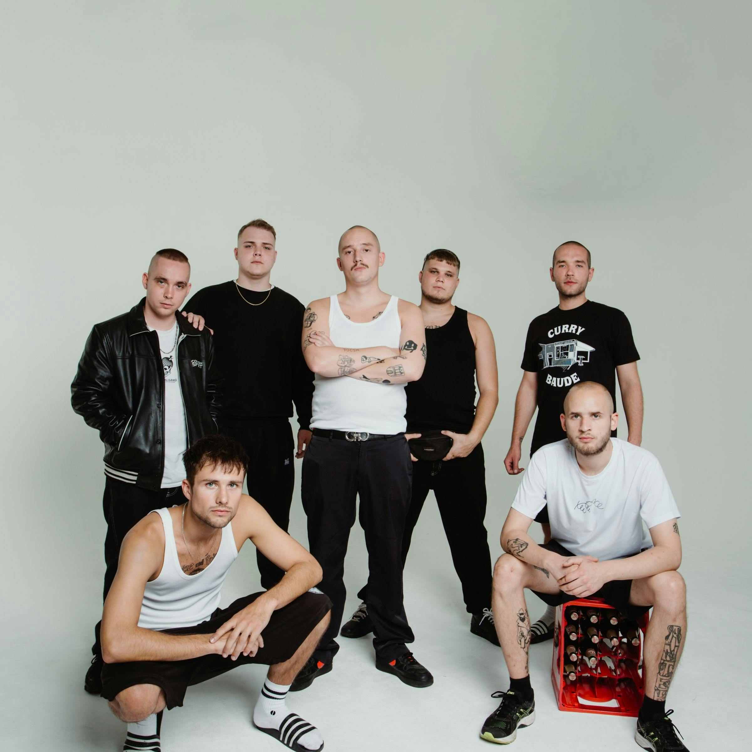 Fünf der sieben Mitglieder der 102 Boyz stehen und zwei hocken vor weißem Hintergrund. Sie sind größtenteils schwarz gekleidet und schauen ernst in die Kamera.