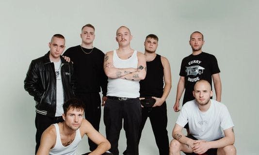 Cinq des sept membres des 102 Boyz sont debout et deux sont accroupis devant un fond blanc. Ils sont principalement vêtus de noir et regardent sérieusement l'appareil photo.