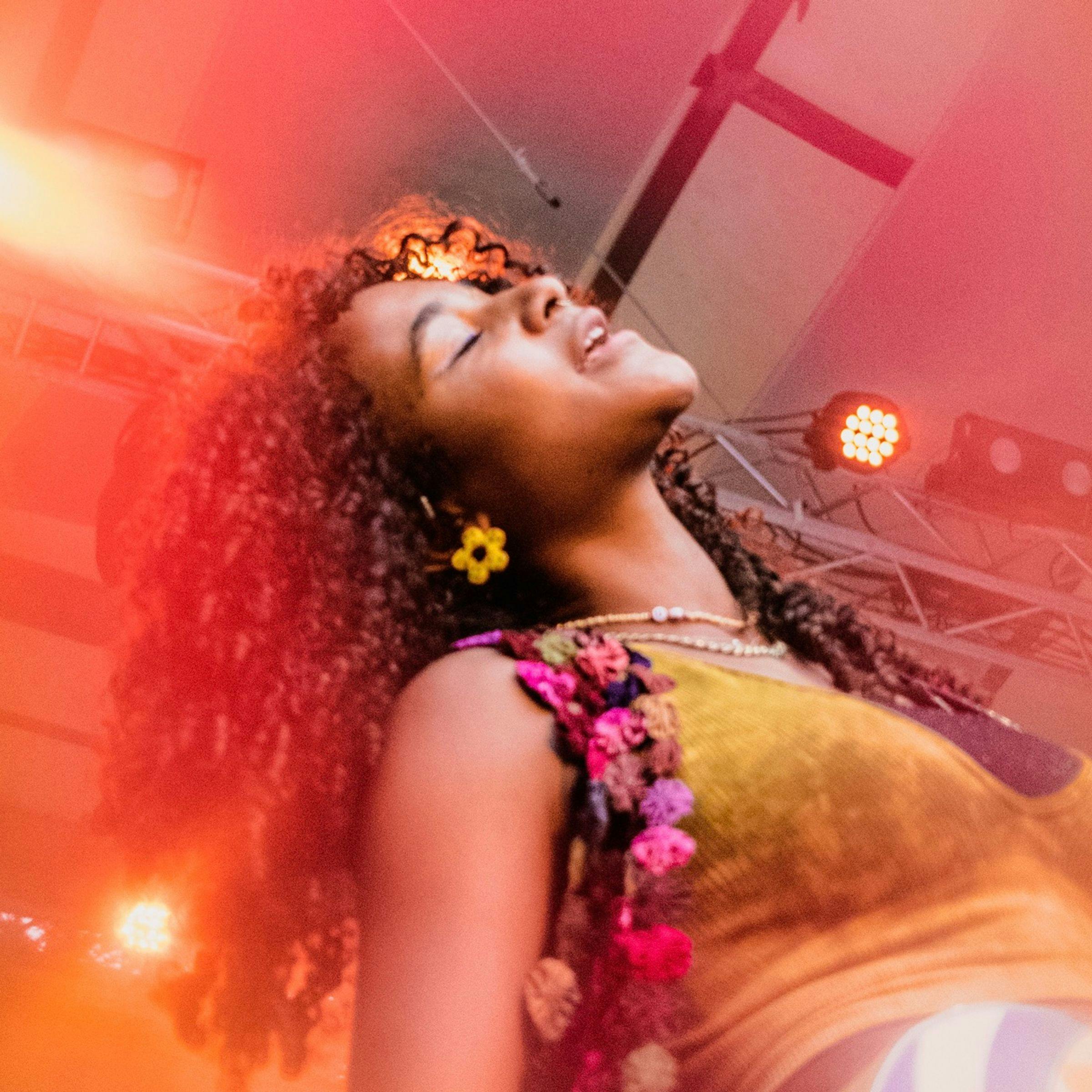 Uche Yara is being photographed from a low angle at one of her concerts. She is singing and has her eyes closed.
