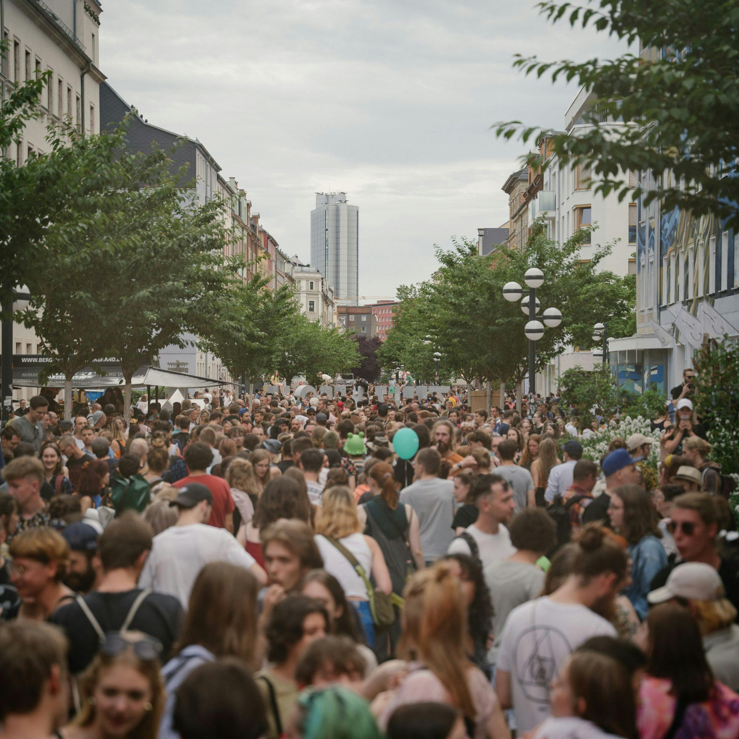 A crowd of people is standing in the streets of Chemnitz looking towards the Dorint Hotel.